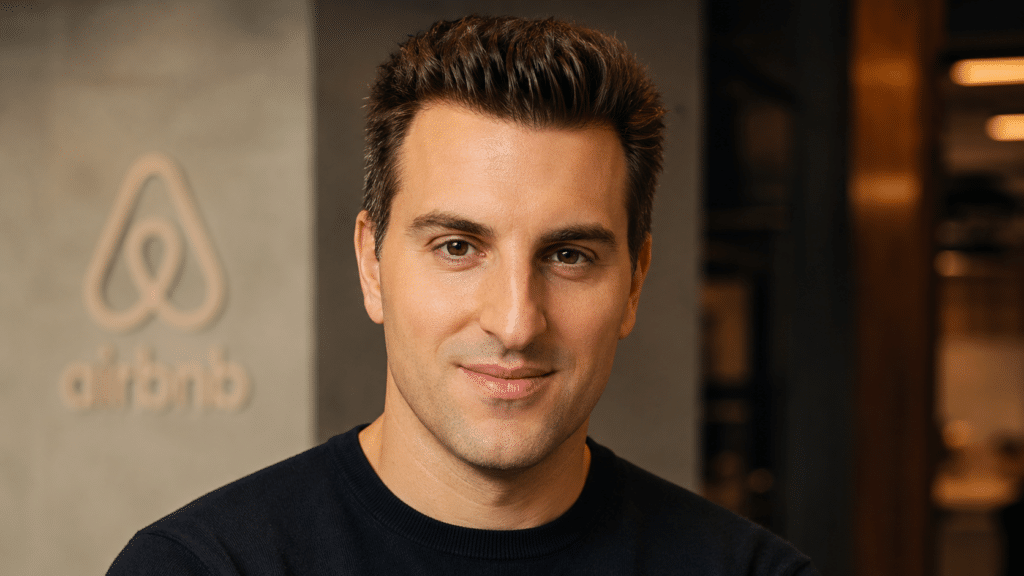 Portrait of a man with dark hair and a black crew-neck sweater, standing in a modern office.