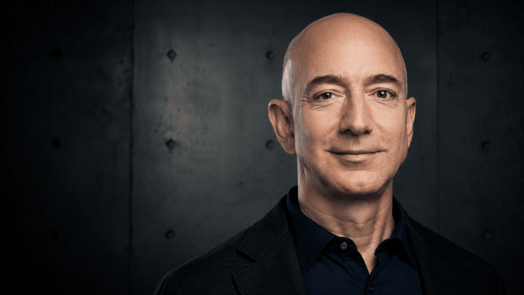 Head-and-shoulders portrait of a smiling bald man in a dark blazer and navy shirt against a moody, textured background.