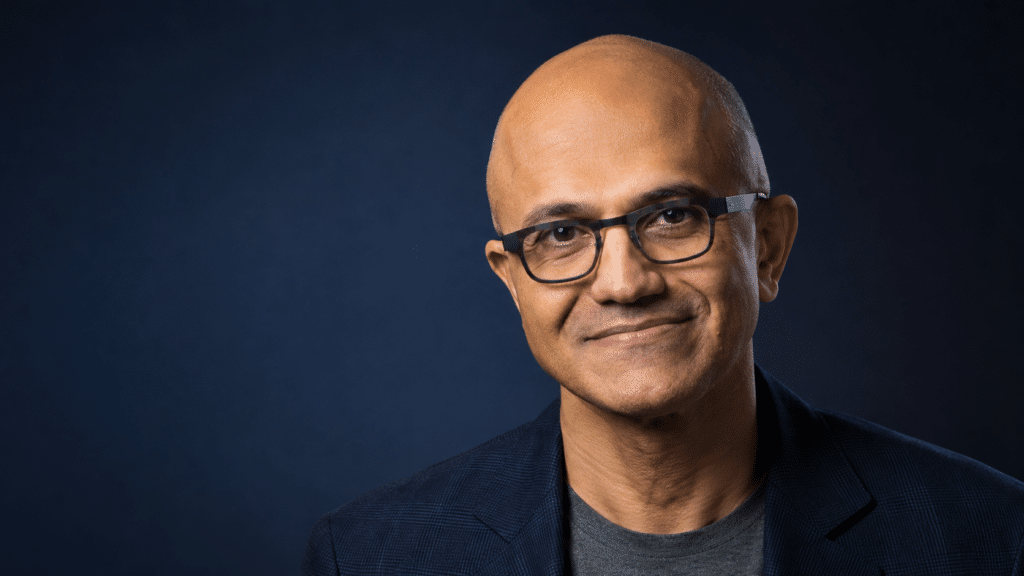 Smiling man with glasses and a dark blazer against a dark blue gradient background.