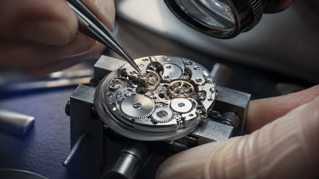 Watchmaker uses tweezers to assemble the intricate gears of a mechanical watch movement in a vise.