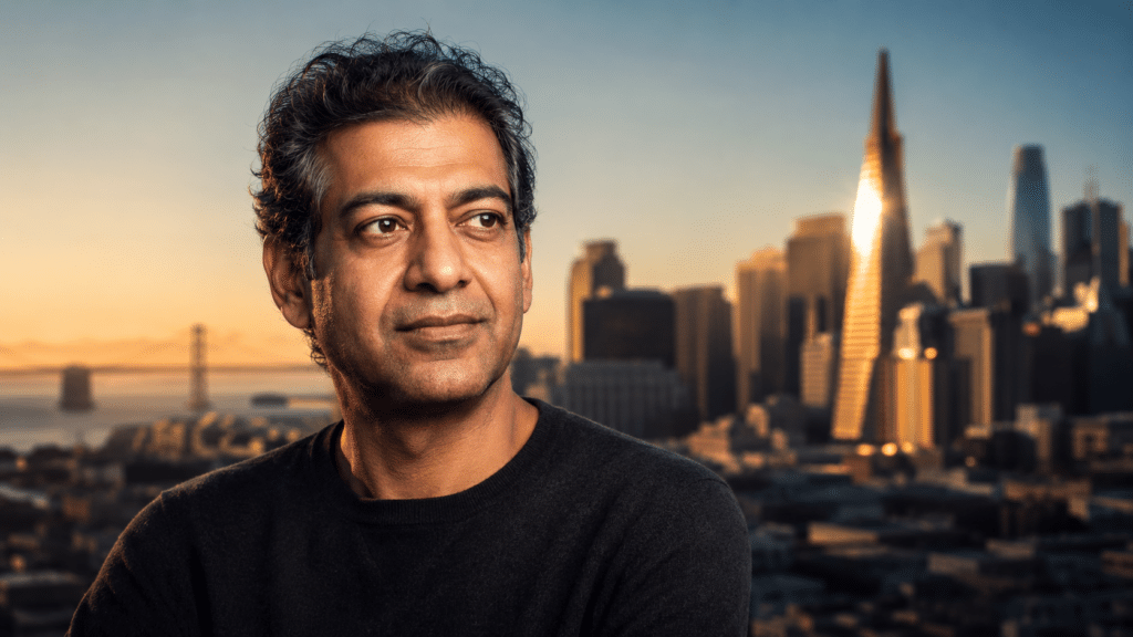 Man in a black sweater gazes off to the side with a sunset city skyline behind him.